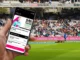 Fan dans un stade regardant son smartphone pendant une rencontre sportive, illustrant une activation en temps réel dans le sport.