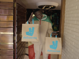 Khaby Lame portant deux sacs Deliveroo sur le pas d'une porte dans le film de la campagne Deliver Us To Fútbol pour la Coupe du Monde 2026