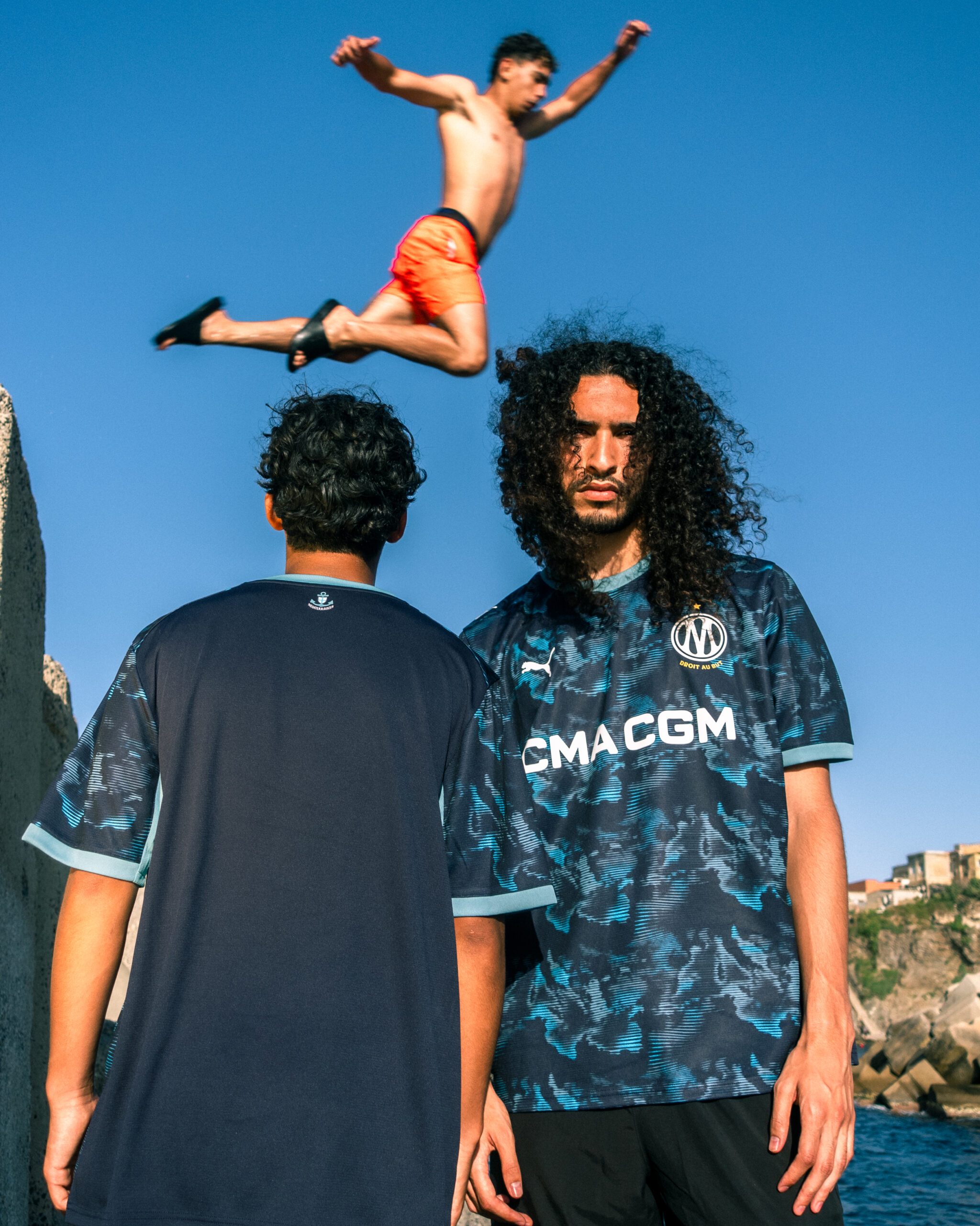 Groupe de personnes sur les rochers, quelqu'un qui saute dans l'eau. Énergie, dynamisme, esprit méditerranéen. Crédit : PUMA × Olympique de Marseille