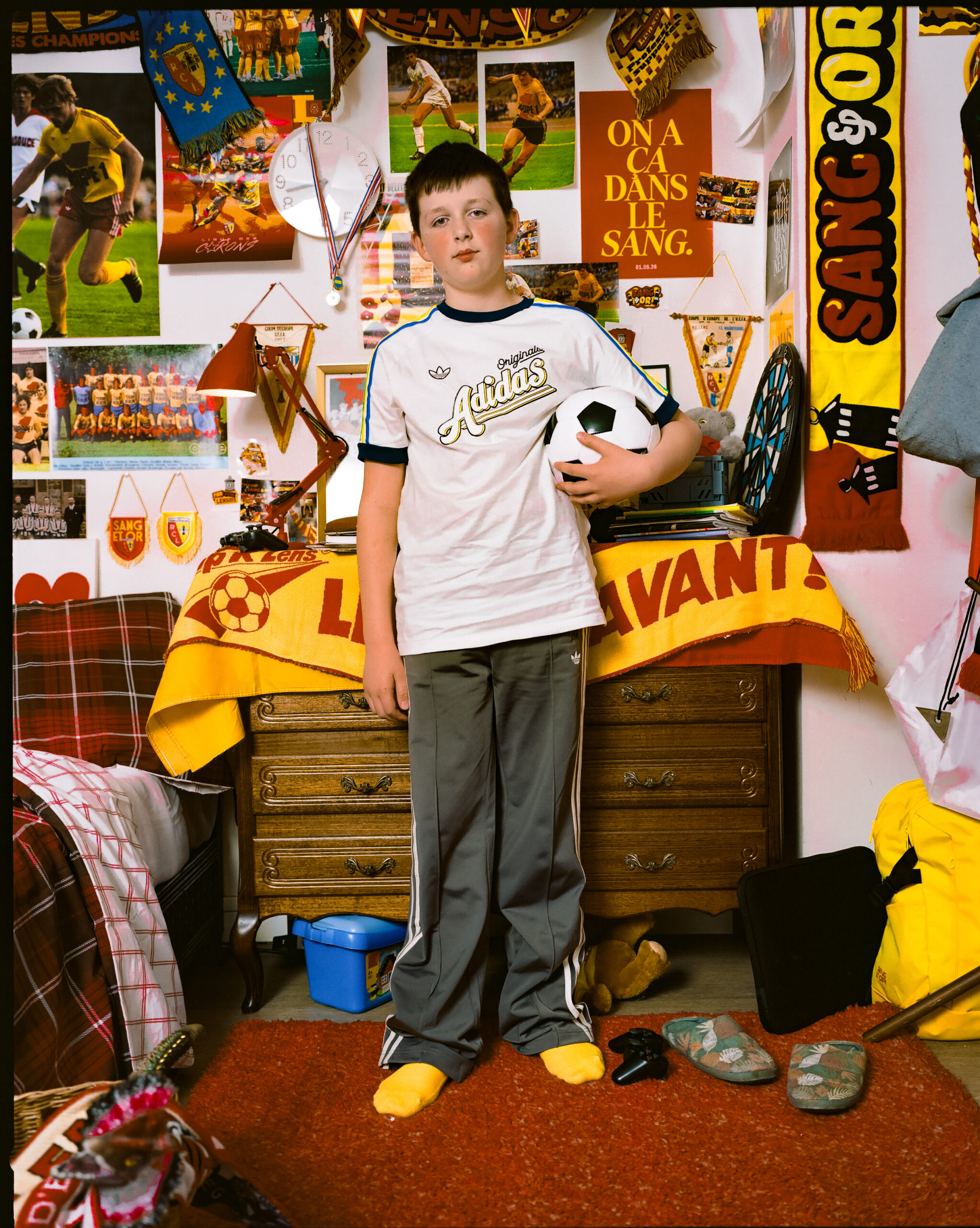 Jeune supporter du RC Lens dans sa chambre décorée aux couleurs sang et or avec un t-shirt adidas Originals
