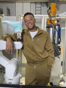 Kylian Mbappé accoudé au bras robotisé qui porte une forme de pied turquoise au On Labs
