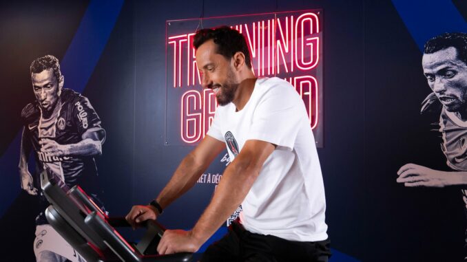 Nenê, légende du PSG, sur un vélo d'appartement dans l'espace fitness Training Ground d'un hôtel Novotel