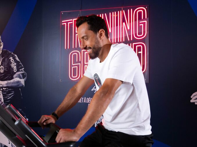 Nenê, légende du PSG, sur un vélo d'appartement dans l'espace fitness Training Ground d'un hôtel Novotel