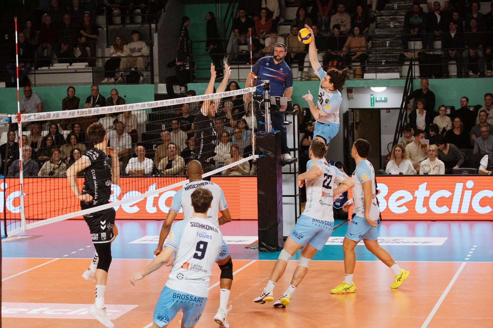 Attaque d'un joueur du Tours Volley-Ball au filet, devant les panneaux lumineux Betclic