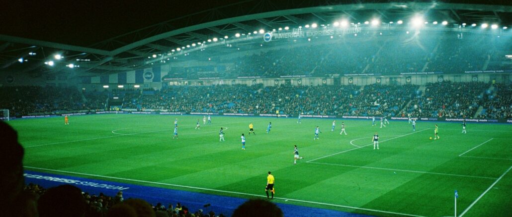Match de football de nuit dans un stade plein, avec des panneaux publicitaires lumineux en bord de terrain, illustration de l’efficacité du sponsoring sportif