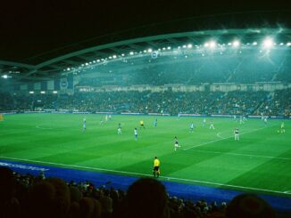 Match de football de nuit dans un stade plein, avec des panneaux publicitaires lumineux en bord de terrain, illustration de l’efficacité du sponsoring sportif