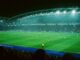 Match de football de nuit dans un stade plein, avec des panneaux publicitaires lumineux en bord de terrain, illustration de l’efficacité du sponsoring sportif