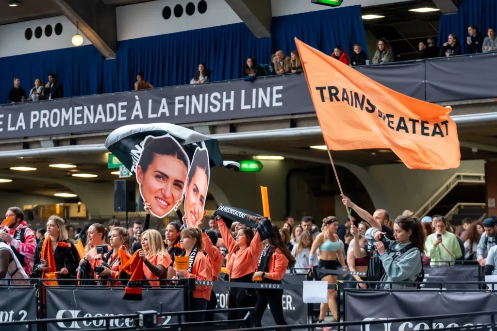 Tribune de supporters Trainsweateat avec drapeau orange et portraits géants à l'HYROX Nice